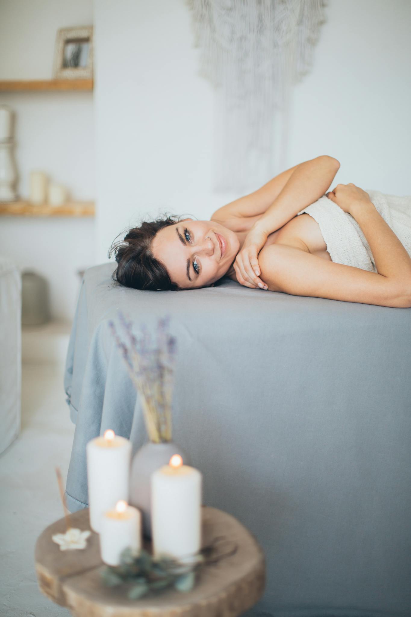 Woman relaxing on a spa bed with candles in a serene setting, conveying tranquility and self-care.
